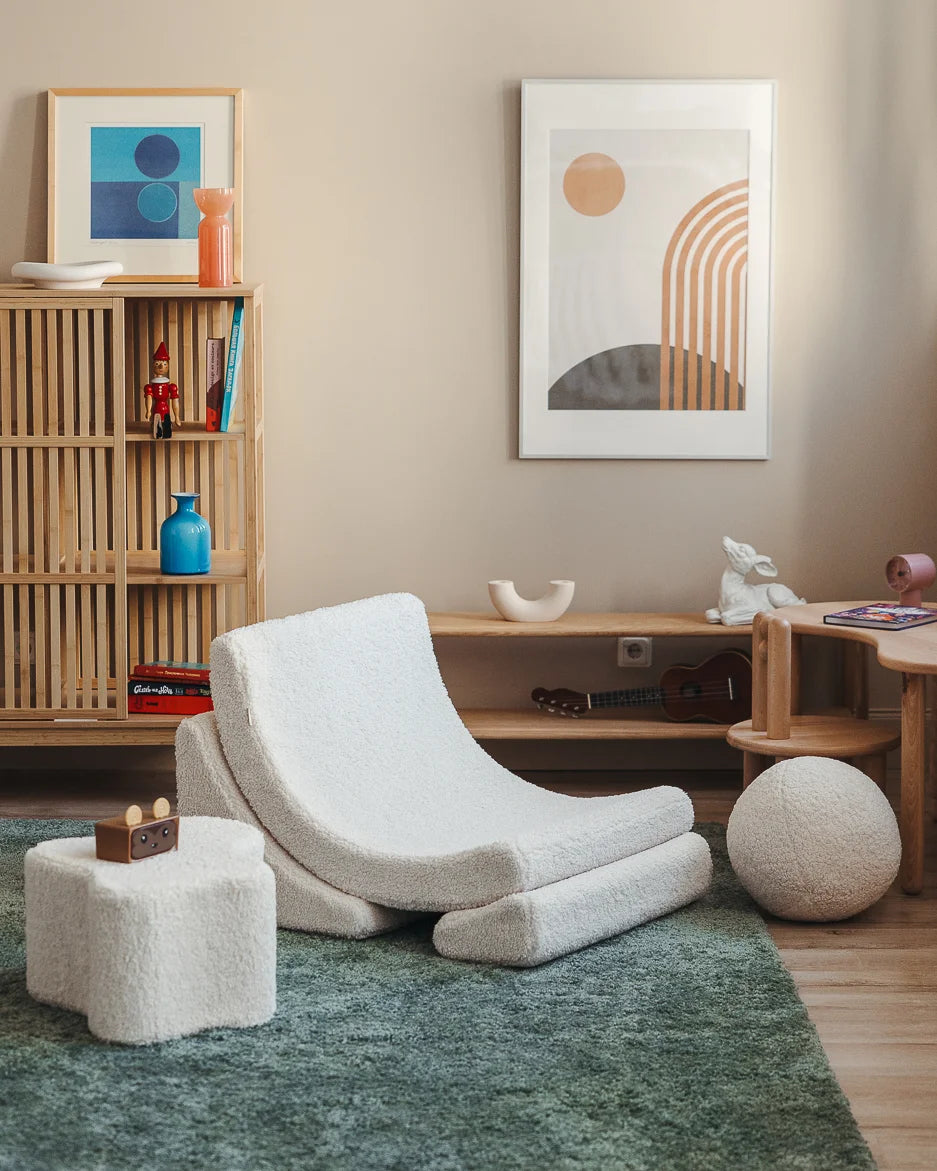 Modern living room with a white curved chair, wooden bookshelf, and abstract wall art.