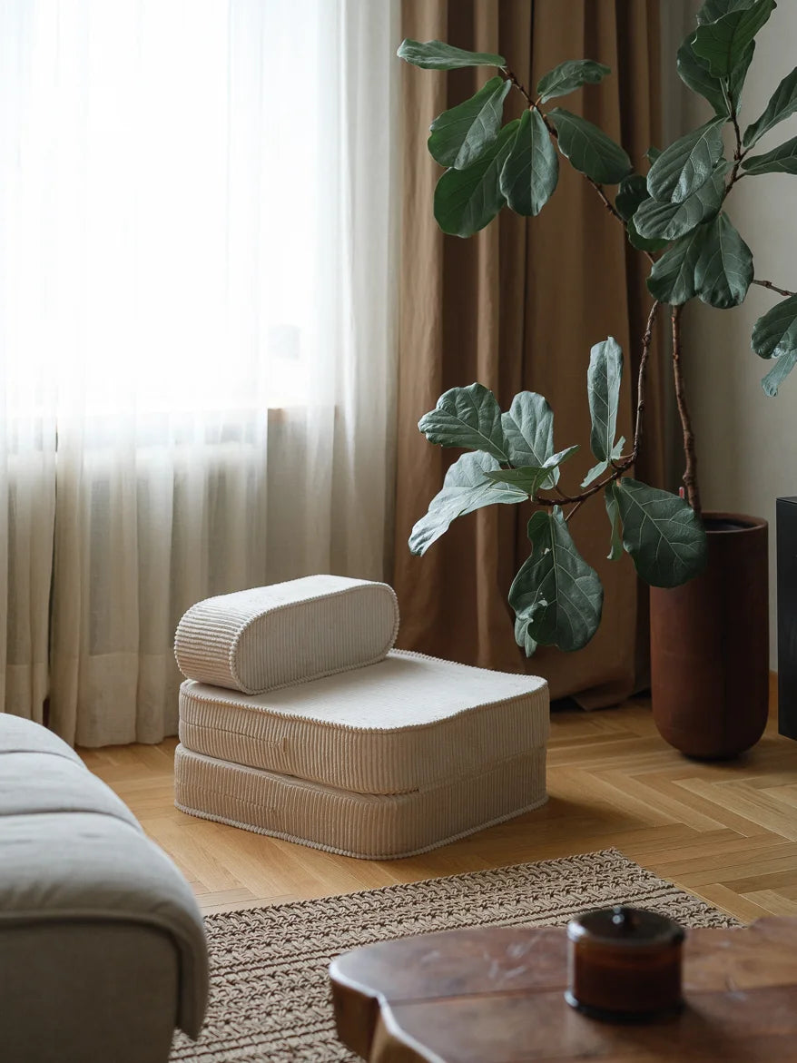 Beige armchair in a living room with a plant and wooden coffee table.