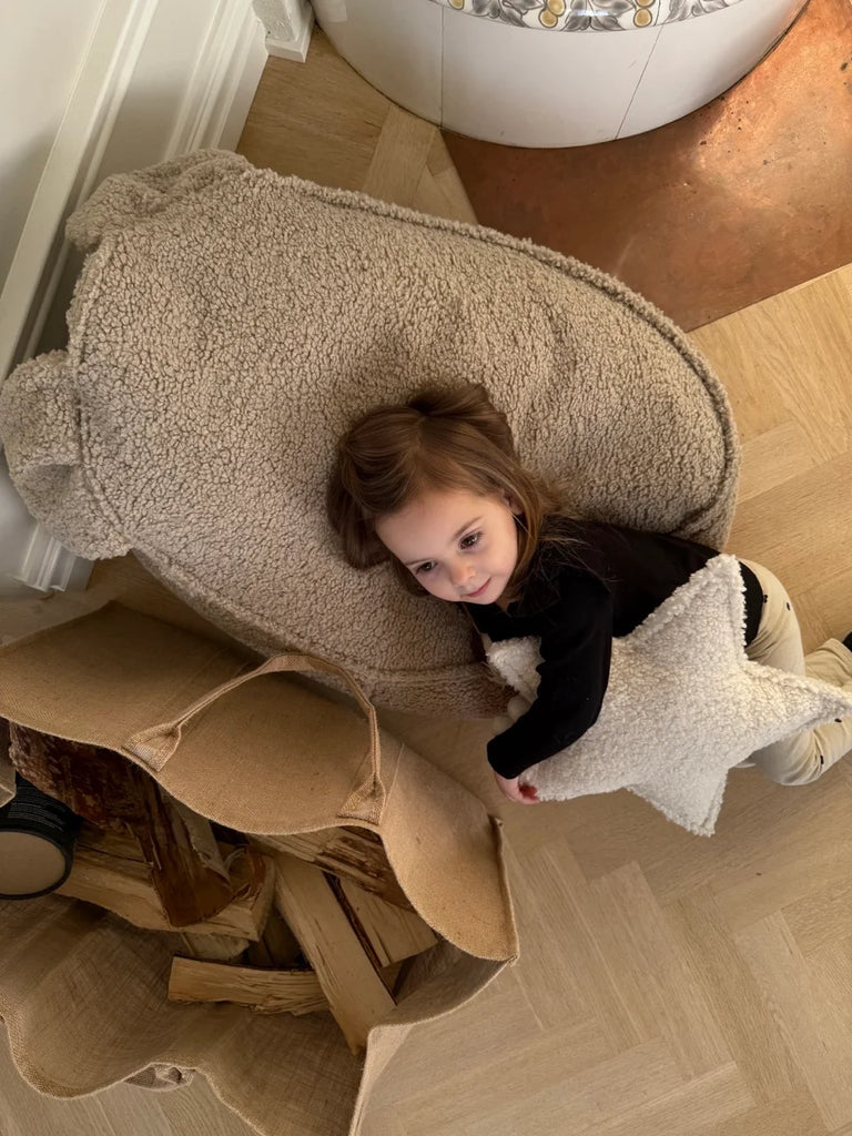 Child resting on a Wigiwama teddy bear beanbag with a star pillow in a cosy corner of a family home