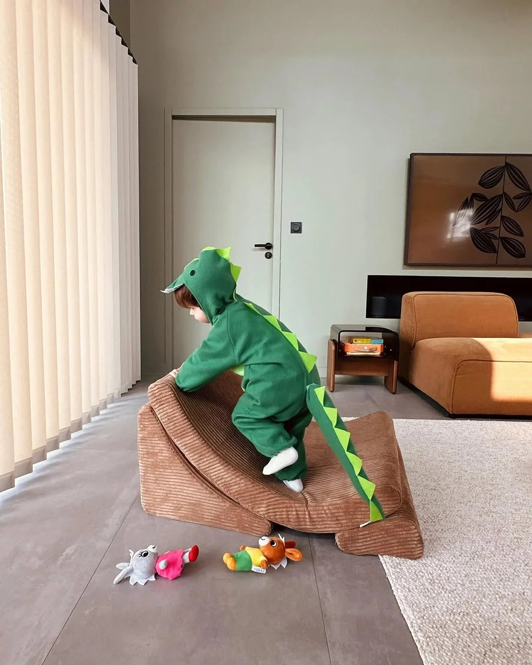 Child in a dinosaur costume climbing a Wigiwama toffee moon chair in a minimalistic home filled with imagination and movement