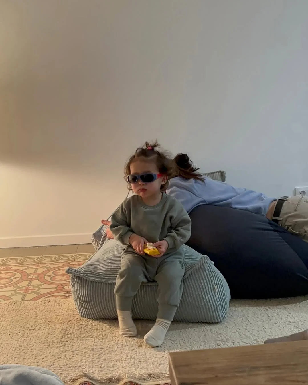 Toddler in sunglasses sitting confidently on a Wigiwama corduroy pouf in a minimalist kids room