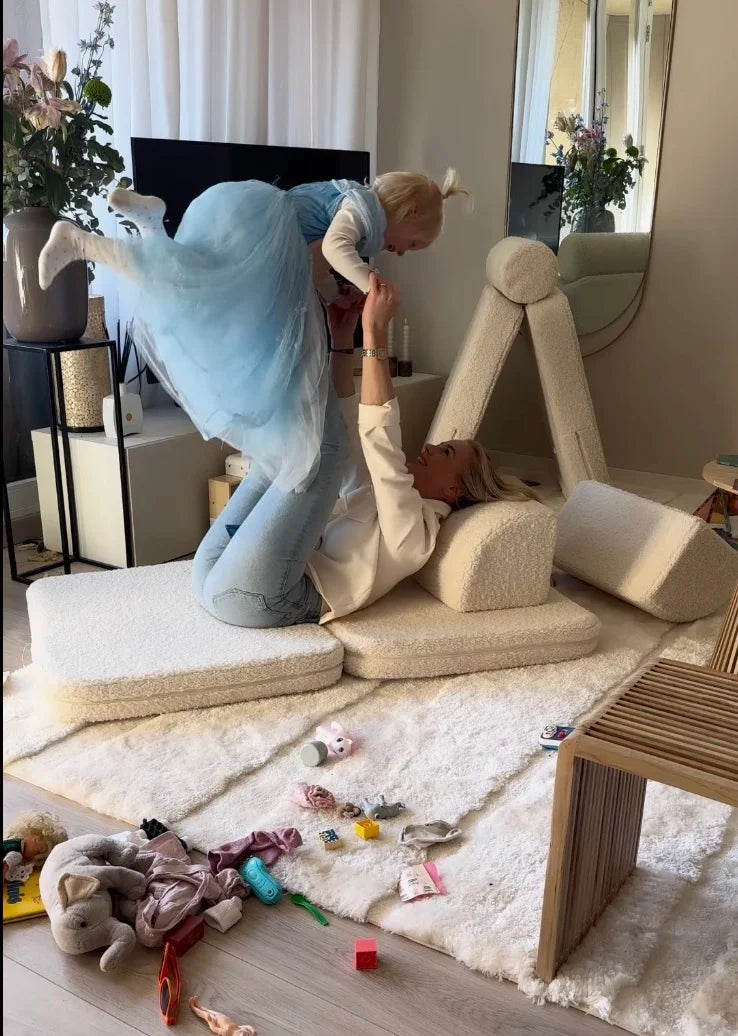 Playful moment between mother and child on a Wigiwama play sofa, surrounded by soft shapes and scattered toys