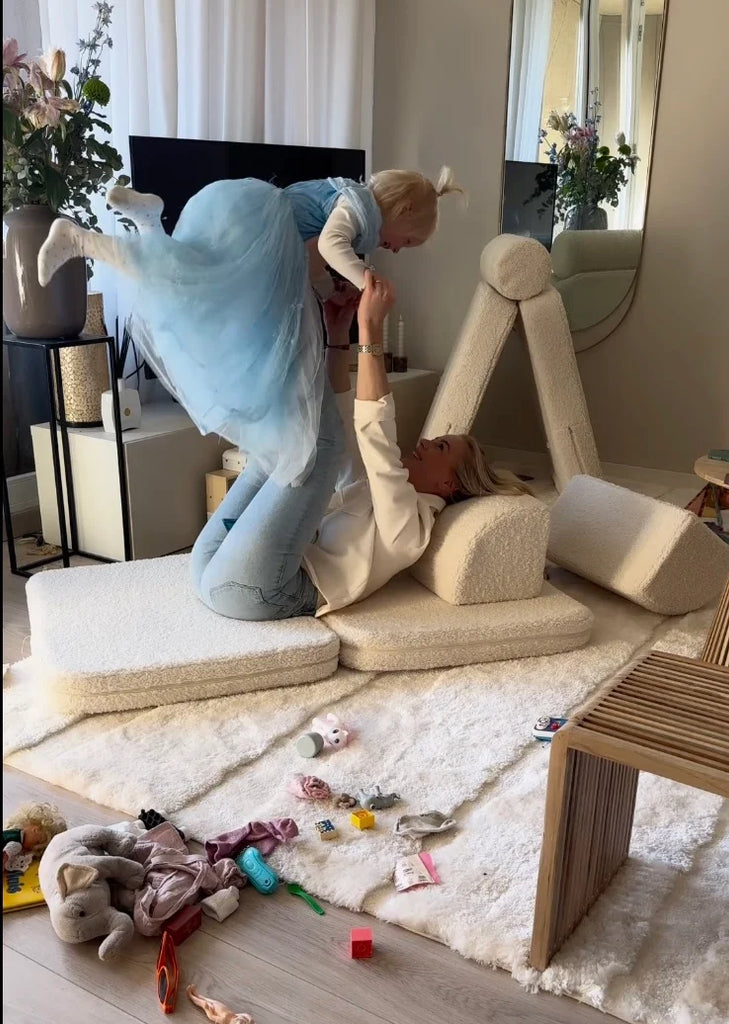 Playful moment between mother and child on a Wigiwama play sofa, surrounded by soft shapes and scattered toys