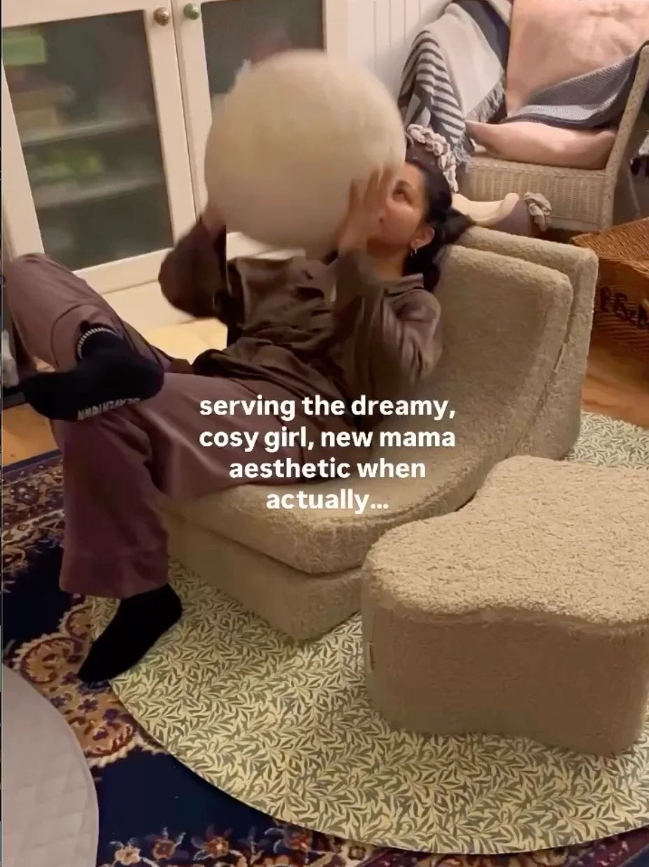 New mom sitting on a teddy Wigiwama Moon chair, holding a ball cushion in a candid, lived-in family room