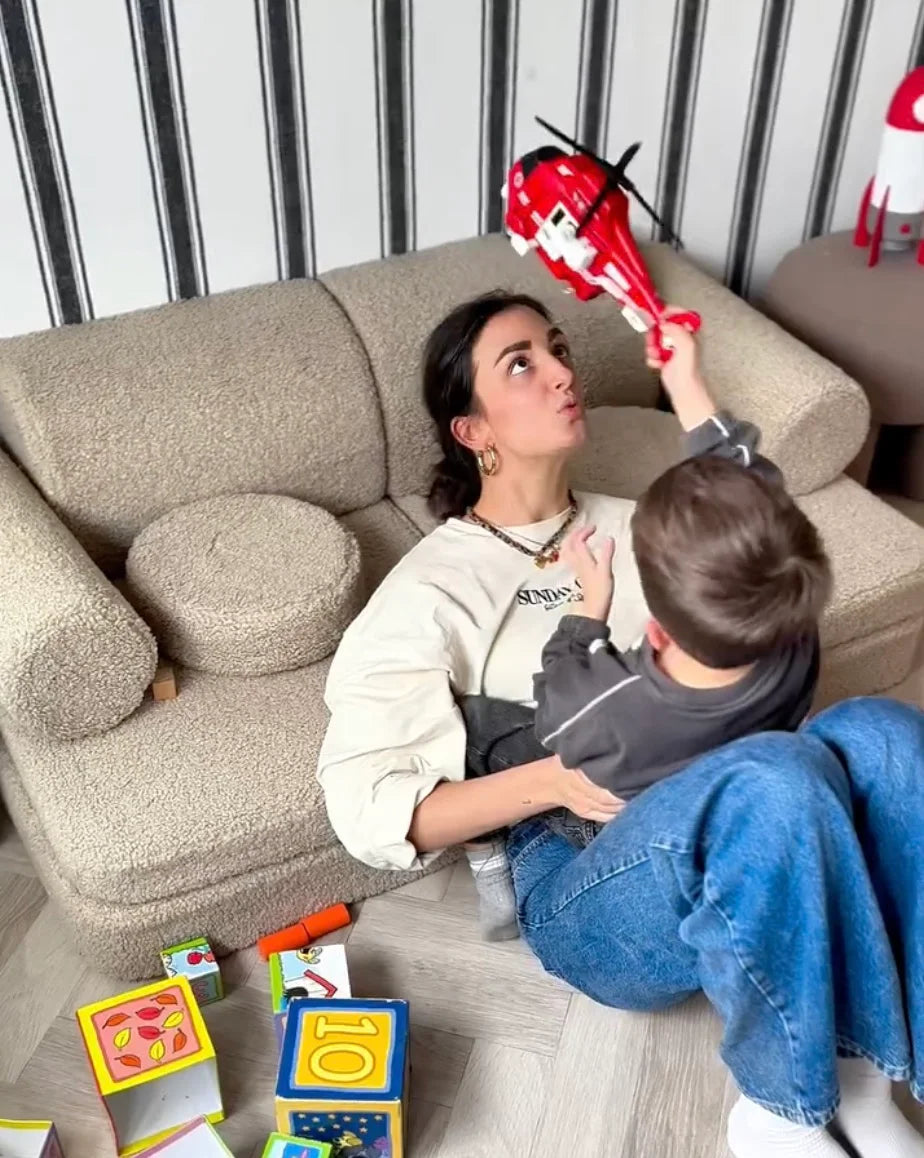 Mother and child playing with a toy helicopter on a teddy Wigiwama sofa in a colourful, toy-filled space