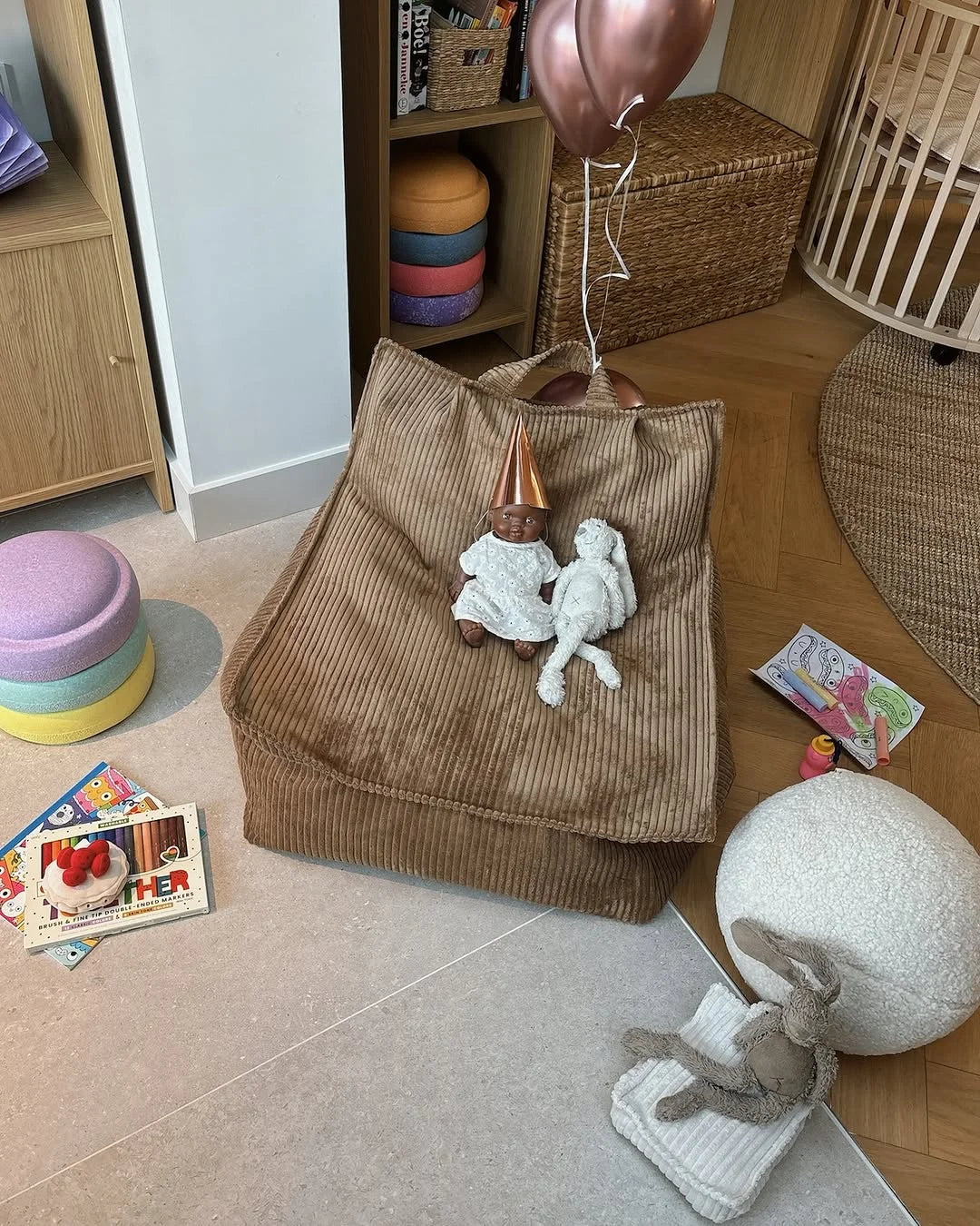 Wigiwama Corduroy beanabag styled with dolls, books, and rainbow stacking bowls in a cheerful corner of a kids room