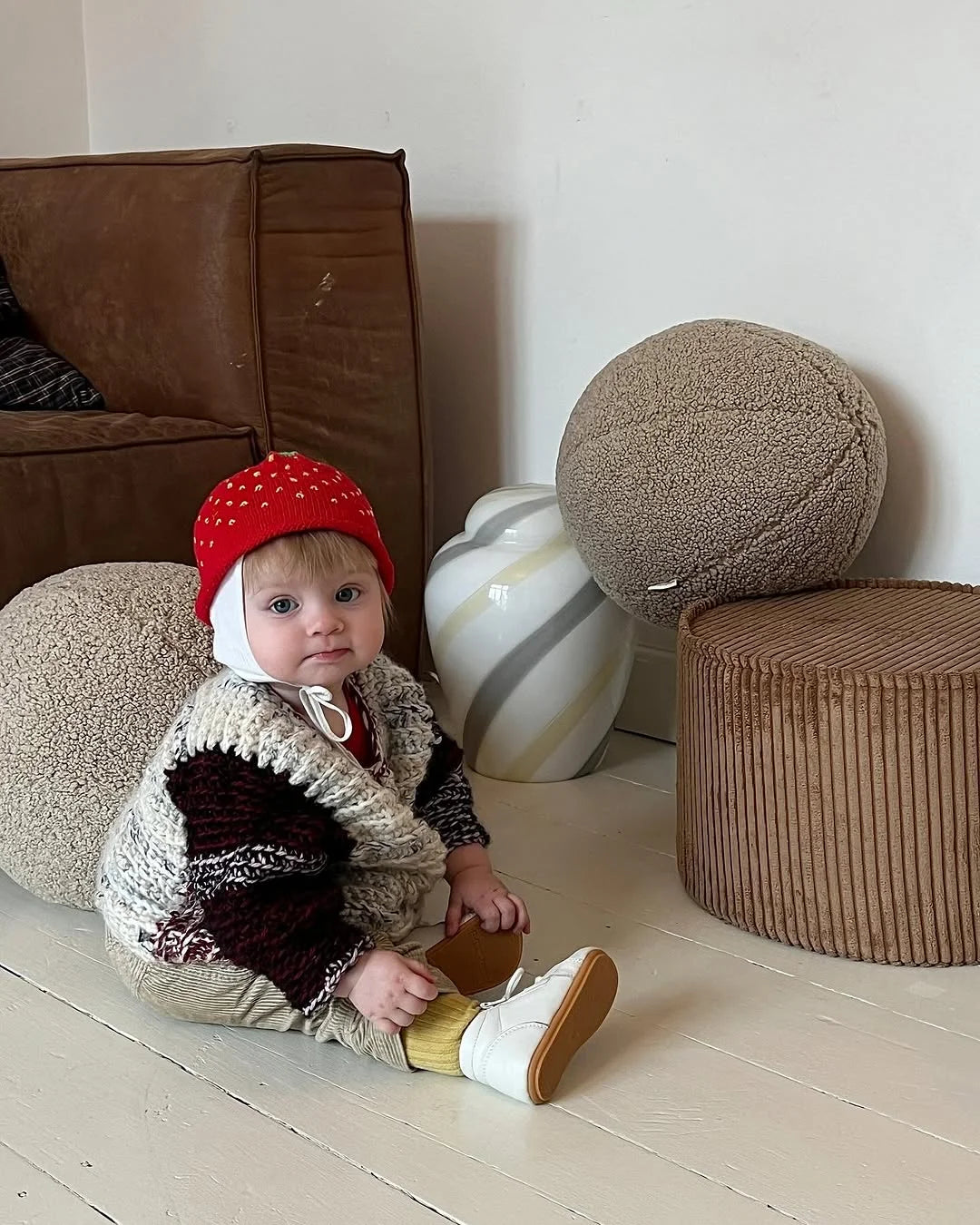 Toddler in a wool vest sitting beside Wigiwama corduroy poufs in a minimal, modern living space