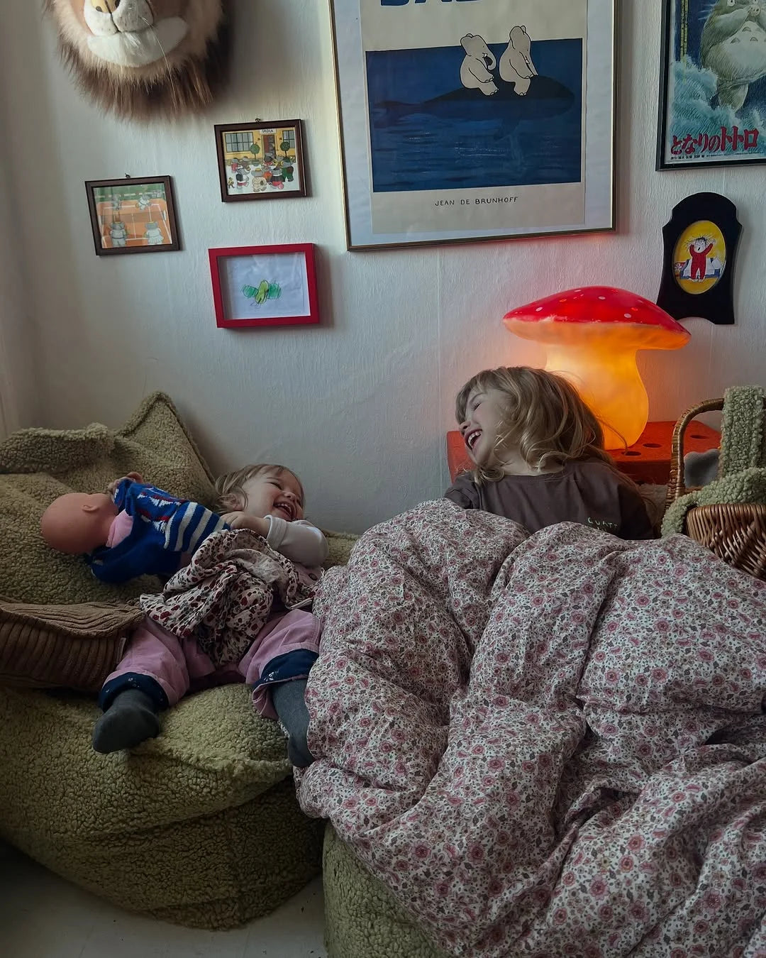 Two children cuddled up on Wigiwama beanbags in a cosy nook under warm lighting and playful wall art