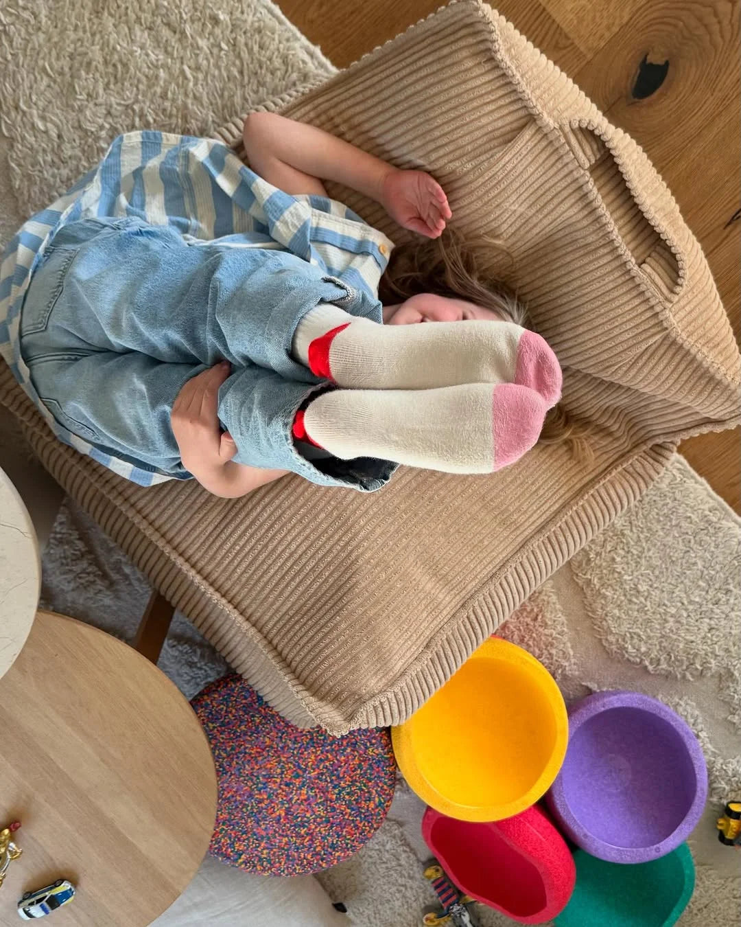 Child playing on a Wigiwama corduroy beanbag in a playful space filled with colourful Montessori toys