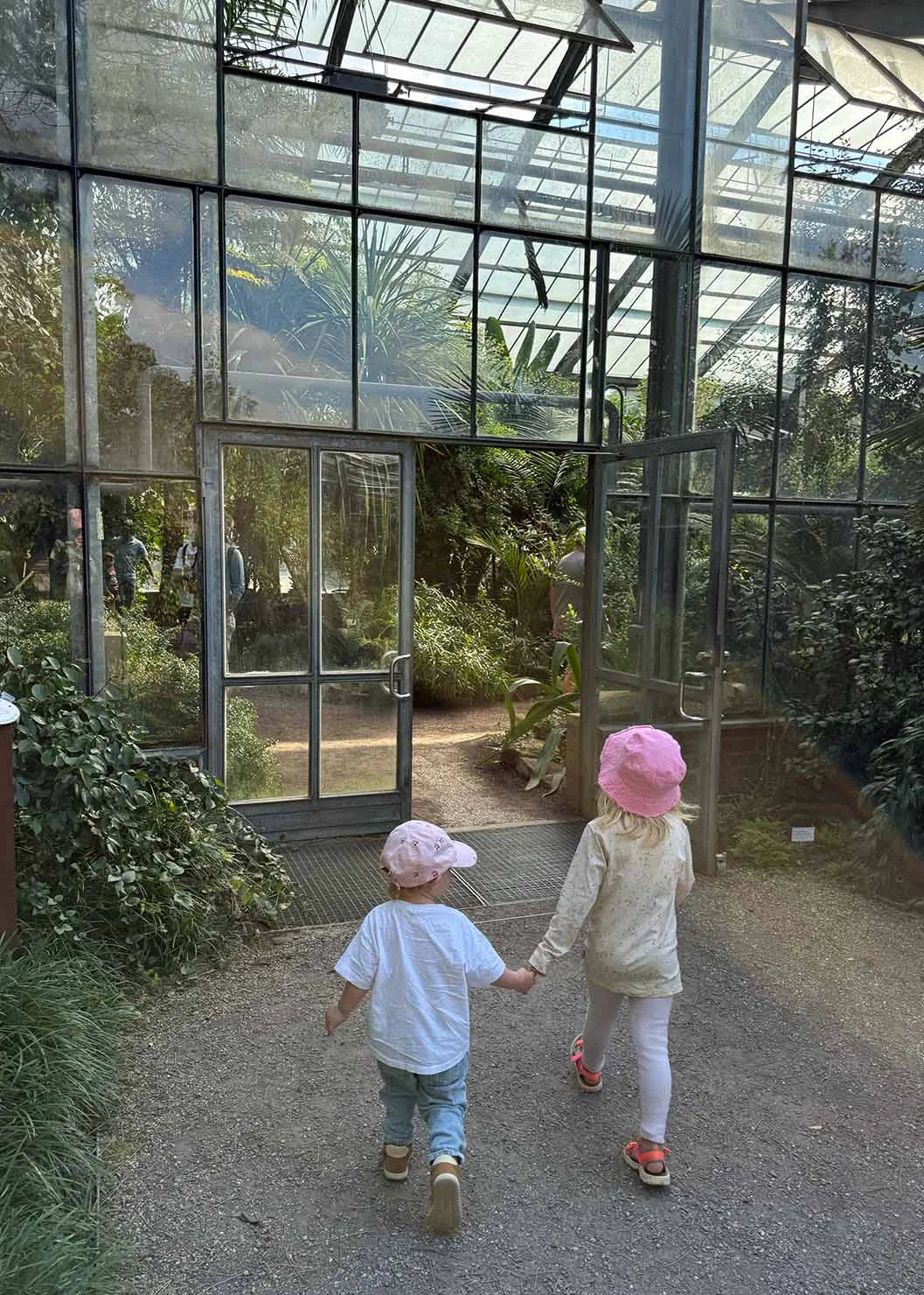 Two children holding hands walk toward the entrance of the greenhouse at the Botanical Garden in Cologne.