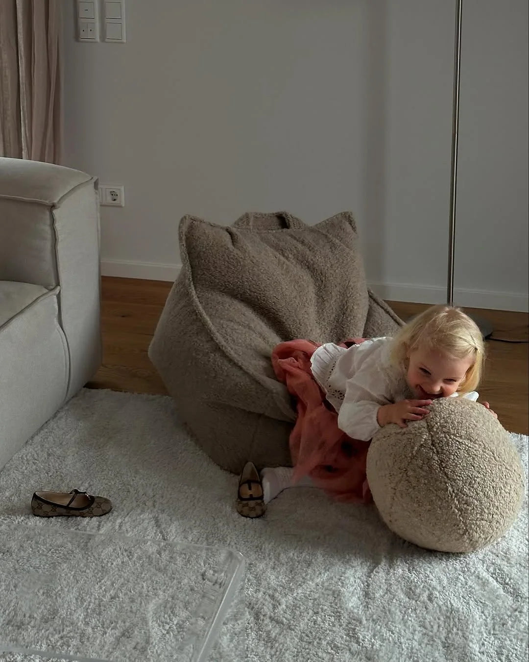 Toddler hugging a teddy Wigiwama cushion on a soft rug in a neutral, minimalist living room