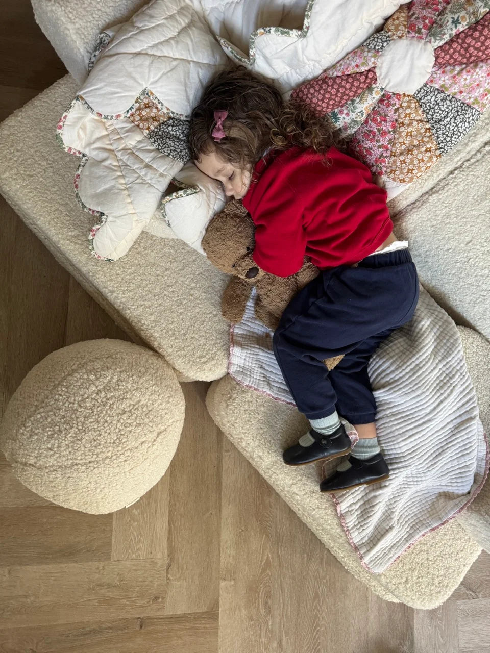Young girl cuddling a teddy bear while napping on a Wigiwama play sofa layered with patchwork quilts