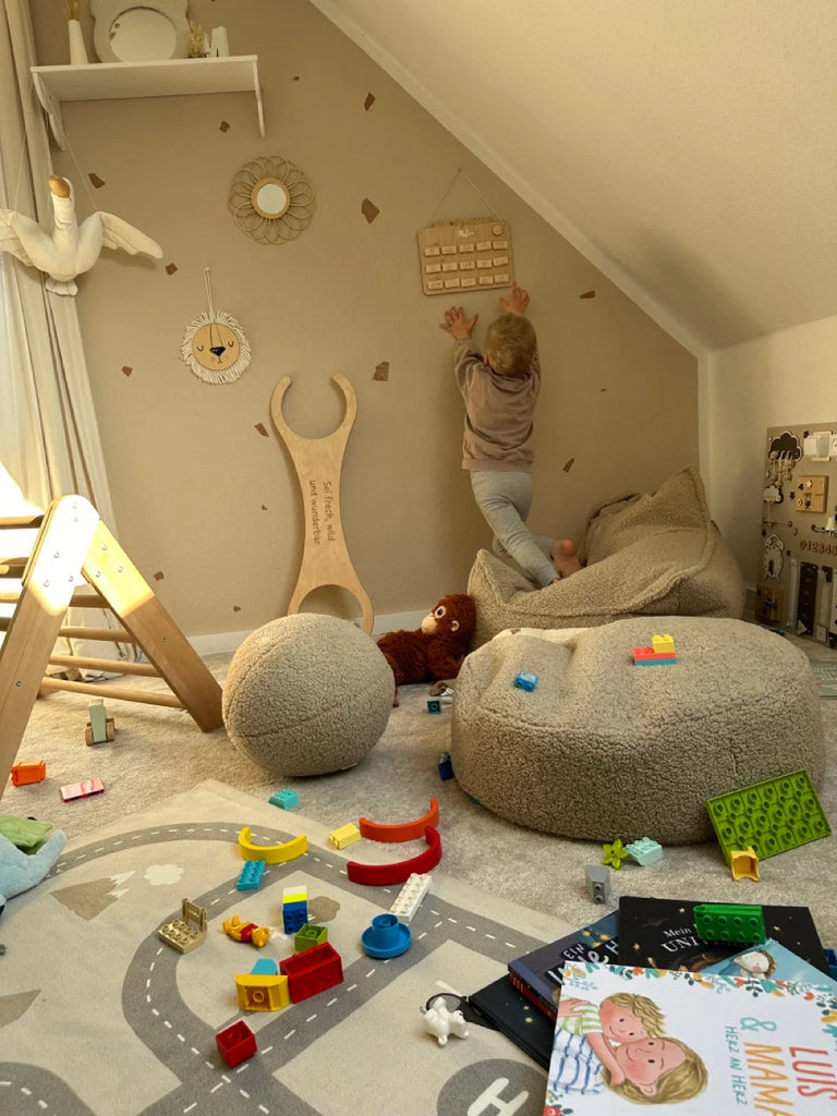 Child climbing on teddy Wigiwama soft play shapes in a toy-filled loft space with cosy textures and wooden details