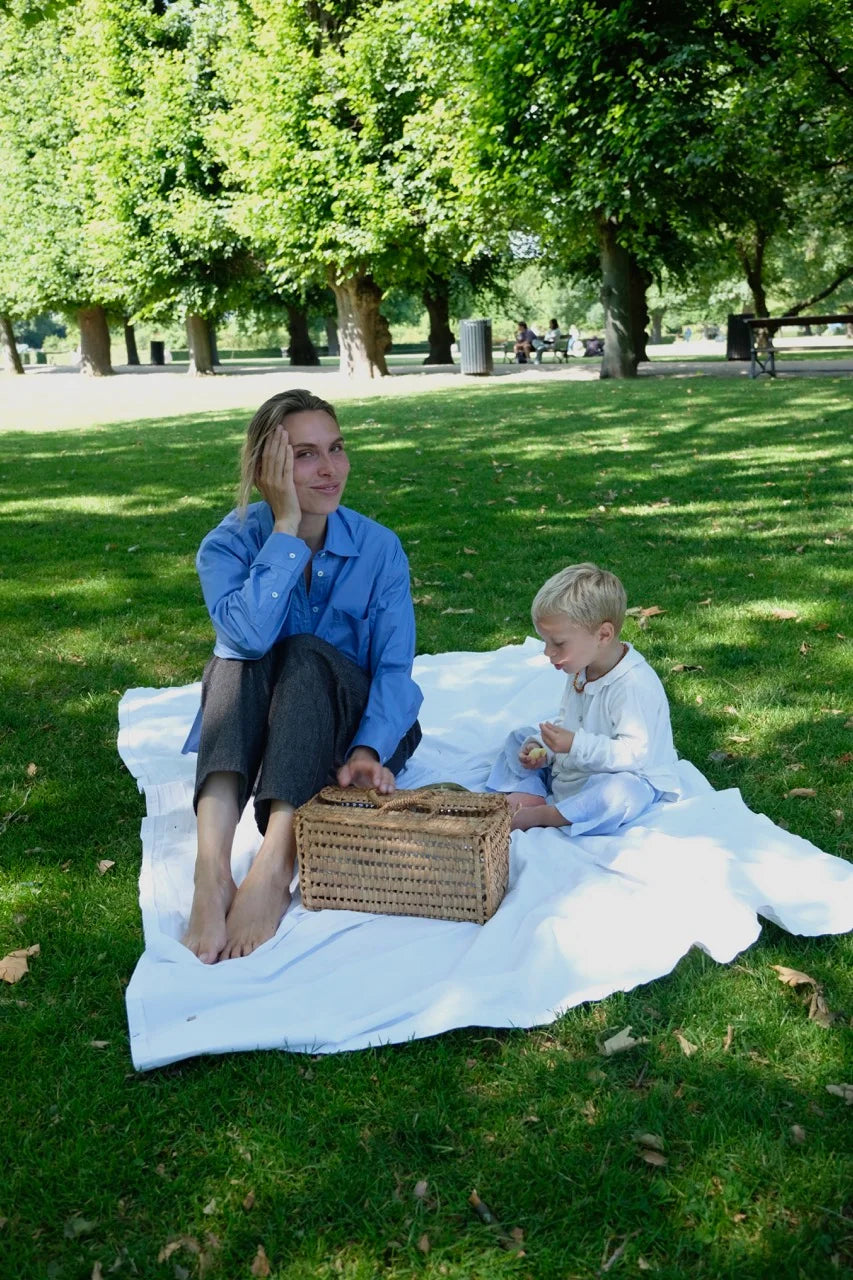 A peaceful picnic scene in a Copenhagen park — a mother and son sit barefoot on a blanket, enjoying the sunshine and snacks.