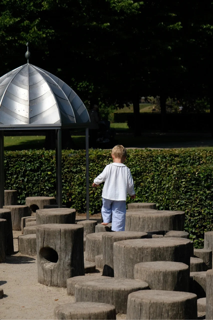A young boy walking barefoot on wooden stumps at a natural playground in King’s Garden, Copenhagen.