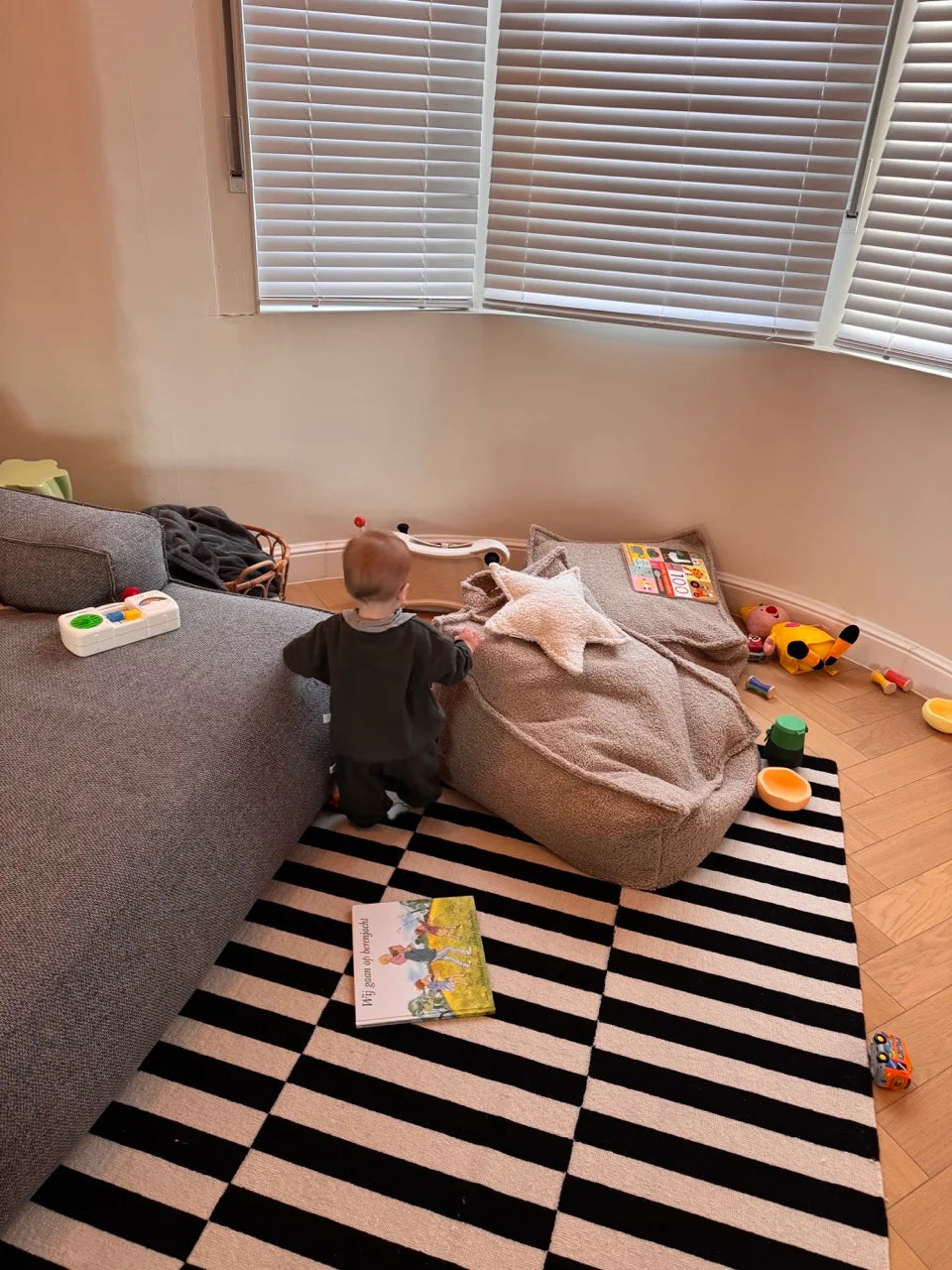 Toddler exploring toys around a Wigiwama beanbag in a real-life play space with books, mess, and warmth