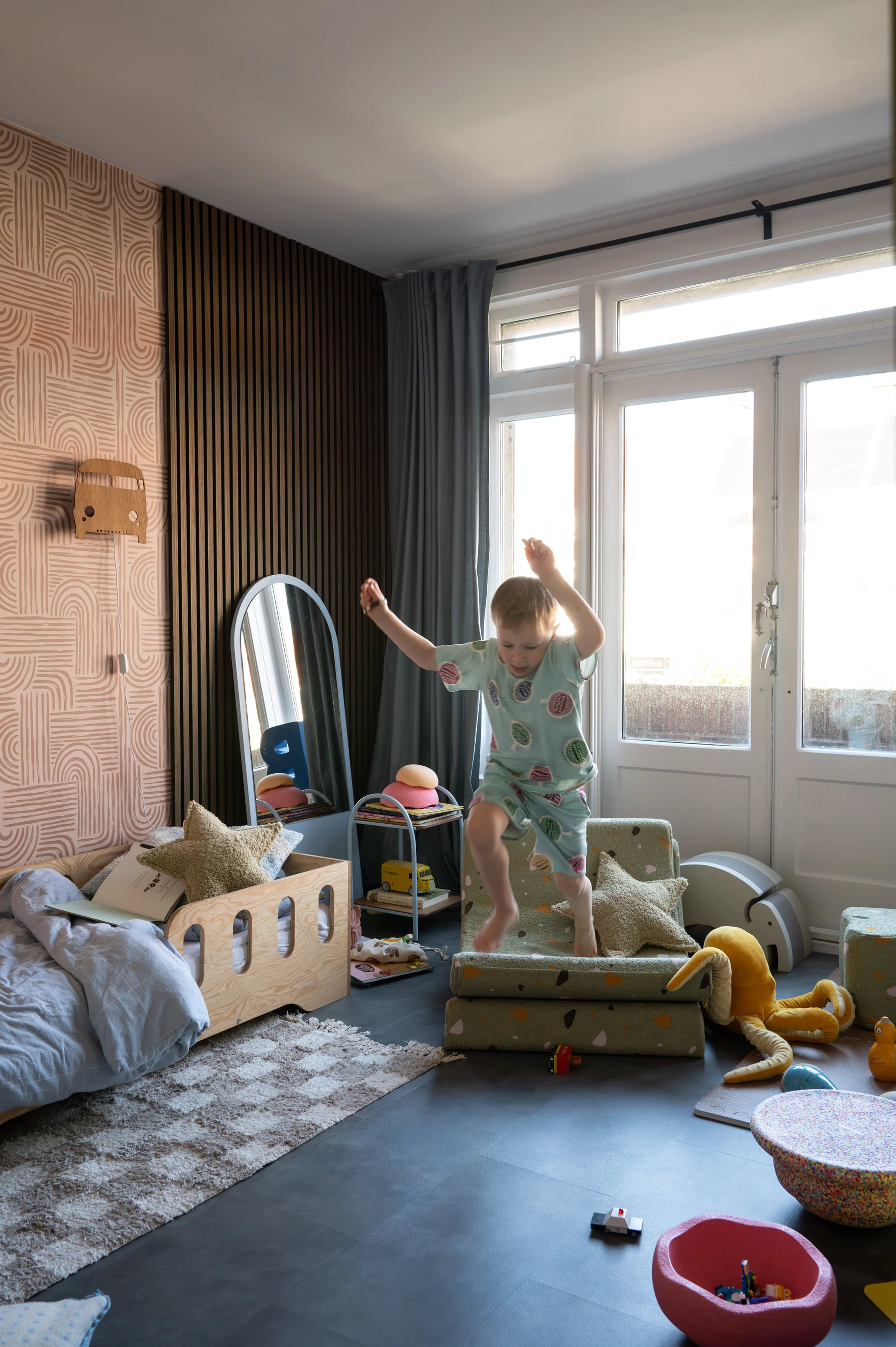 Child jumping joyfully on a Wigiwama Terrazzo Moon Chair in a vibrant kids room with natural light and playful textures