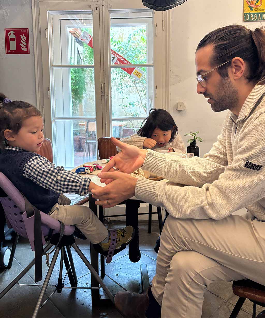 Man sitting with two children at a table in a room with large windows.