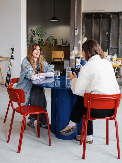 Zane and a team member in conversation at a bold blue table in her studio, surrounded by set materials.